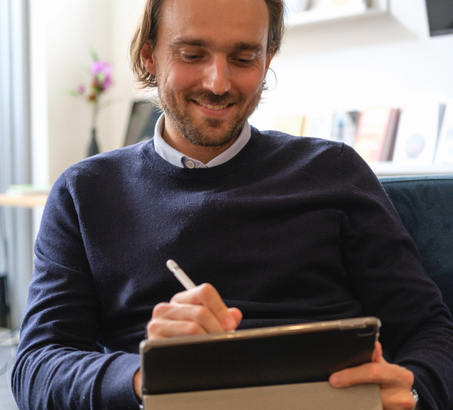 a man is smiling and working on a tablet with a pen